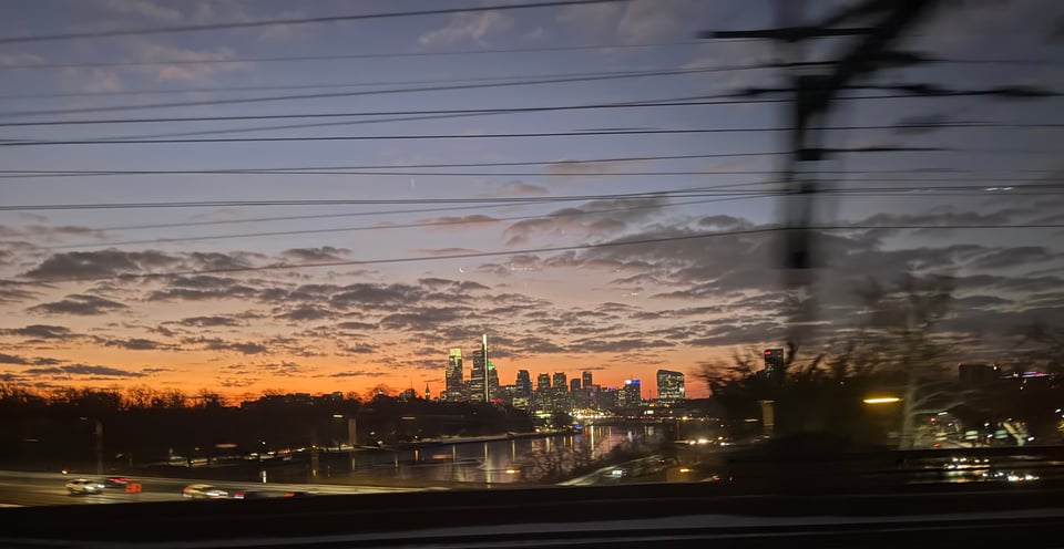 photo of early morning Philadelphia skyline from a train. In the foreground, details are blurry because of the train's motion