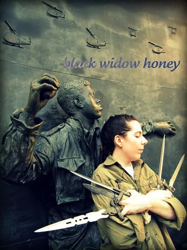 a person stands in profile in front of a statue of a man throwing a grenade. they are wearing what looks like army fatigues, and are looking down while holding five daggers of varying sizes, all pointing outward. it’s filtered with a greenish vintage film.