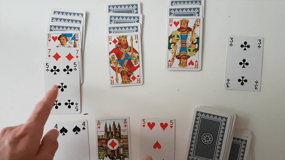 A deck of cards arranged in three columns with the royal cards face-up. A hand is visible in the lower left, pointing at one of the columns.