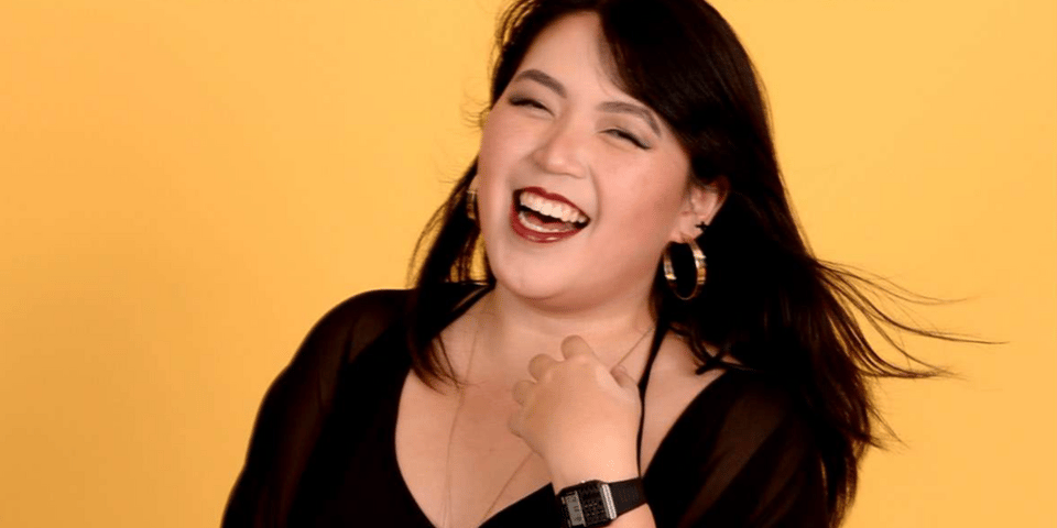 Aih laughing, in front of a yellow background.