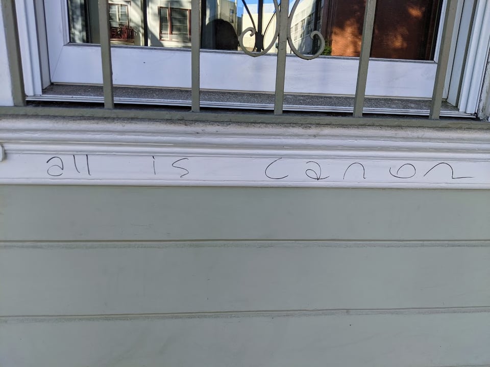 A photo I took of a windowsill under a barred window. Someone wrote the phrase "all is canon" on the windowsill.