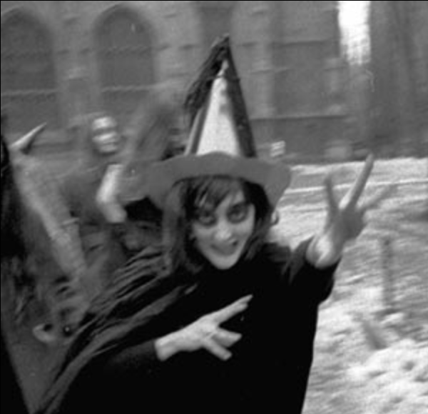 a black and white photo of a woman dressed as a halloween witch dancing and gesturing menacingly