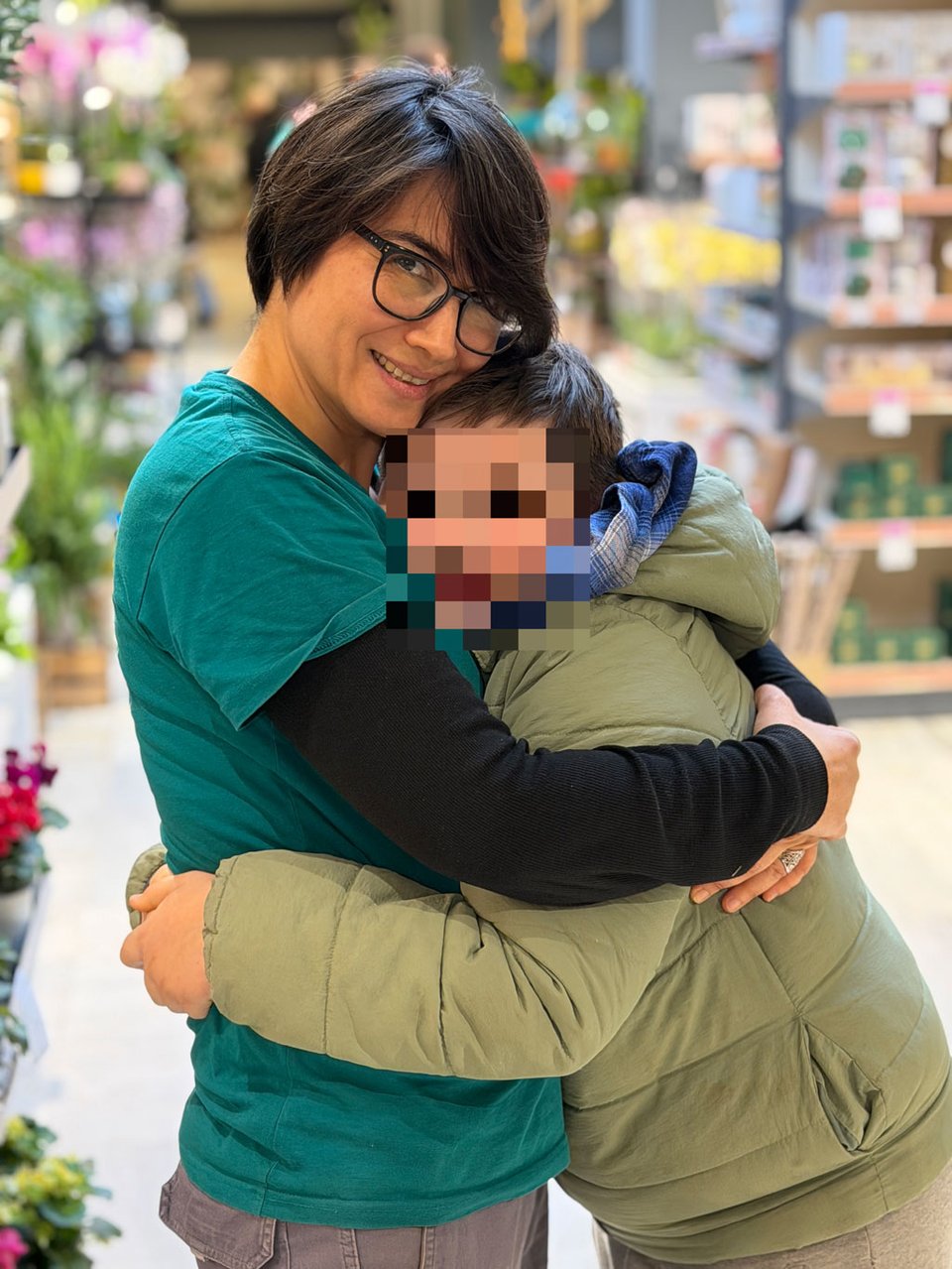 A woman and a young boy hug goodbye. She is looking at the camera. The young boy's face is blurred.