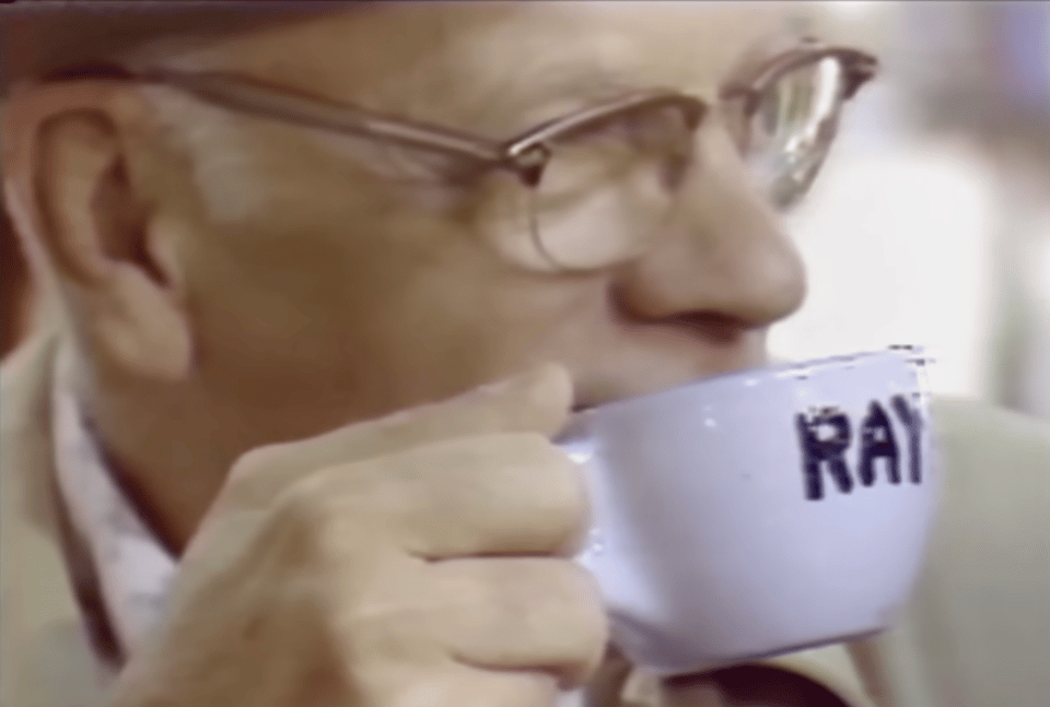 A man in glasses drinking from a coffee cup with his name 'Ray' written on it