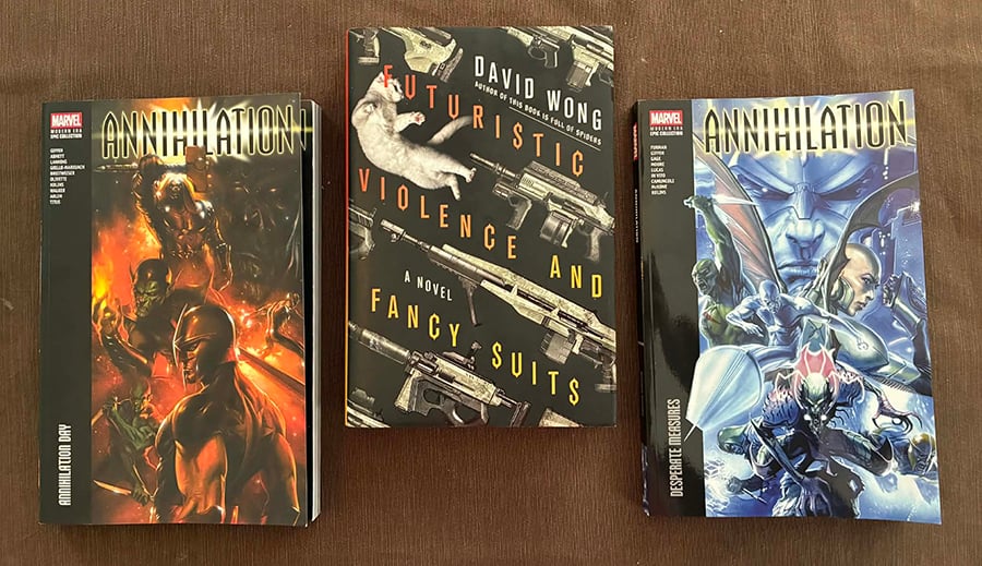 The books Annihilation volume 1, Futuristic Violence and Fancy Suits, and Annihilation volume 2 sitting on my dining room table. There is a brown tablecloth.