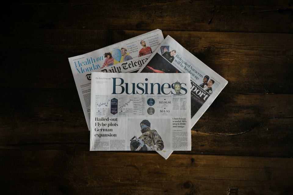 Three newspaper sections, stacked on a table. The topmost is the business section. Photo by Annie Spratt on Unsplash.