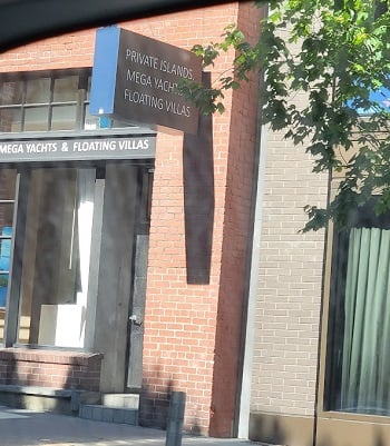 Photo of the front of a business that has a sign that says, “Private Islands, Mega Yachts, Floating Villas.”