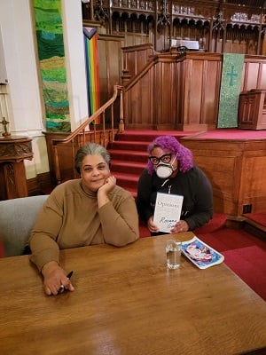 Roxane Gay and Patricia aka The Infophile at Roxane Gay’s book signing in a church. Patricia is wearing a mask and holding up a copy of Roxane Gay’s new book titled Opinions.