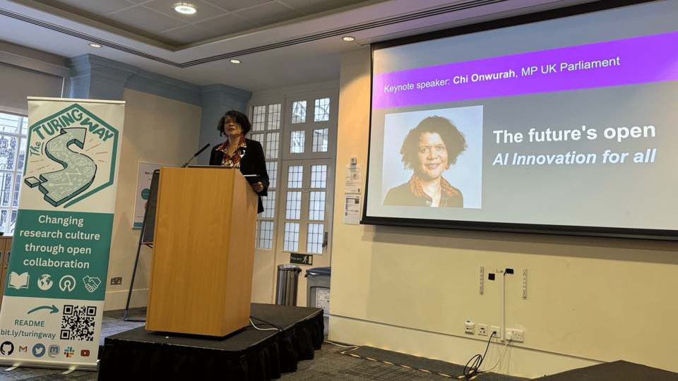 A black woman (Onwurah) stands at a podium with a banner for