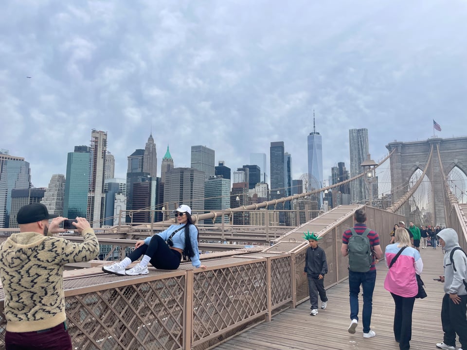 a man taking picture of a woman posing on the deck of the Brooklyn Bridge