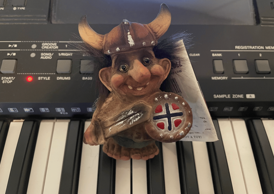 A Troll with a viking helmet stands on a keyboard, staring with little jewel eyes