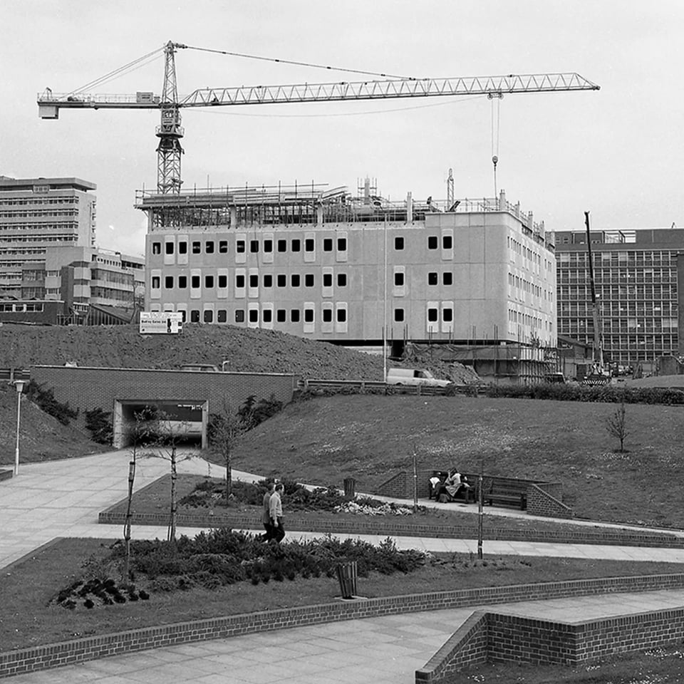 A long shot across the North Cross pedestrian underpass at the top of Armada Way in the early 1970s. Beyond it, a concrete frame building is rising. Some, but not all, of the fitted panels have hoods in a rather random pattern.