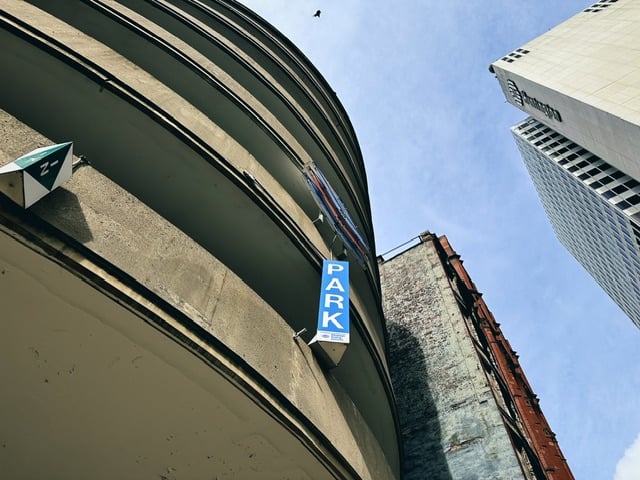 A view of a round parking garage in Pittsburgh, the sky, a couple other buildings, and what’s probably a pigeon flying around.