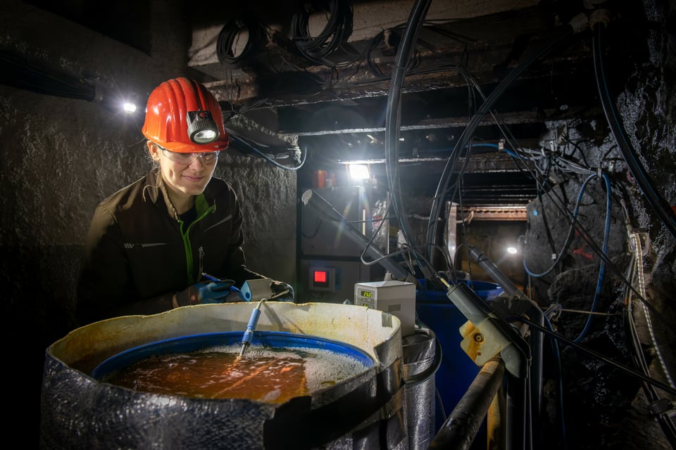 A scientist looking at a plastic bin full of tailing water that looks a little like a cauldron of soup, except that it's in a mine and has some metal probes going into it