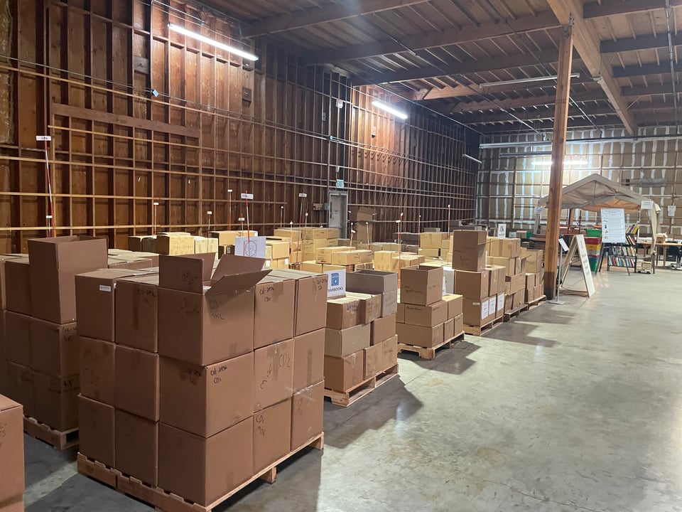 Rows of boxes stacked on pallets sit in front of containers in a warehouse. It's immense.