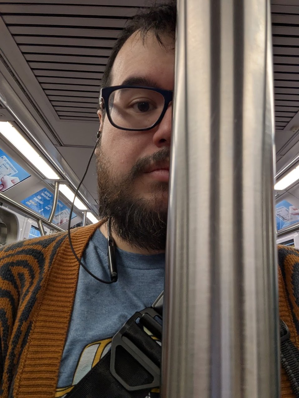 A selfie of Mikkel on the NYC subway, half of their face obscureb by a metal pole.