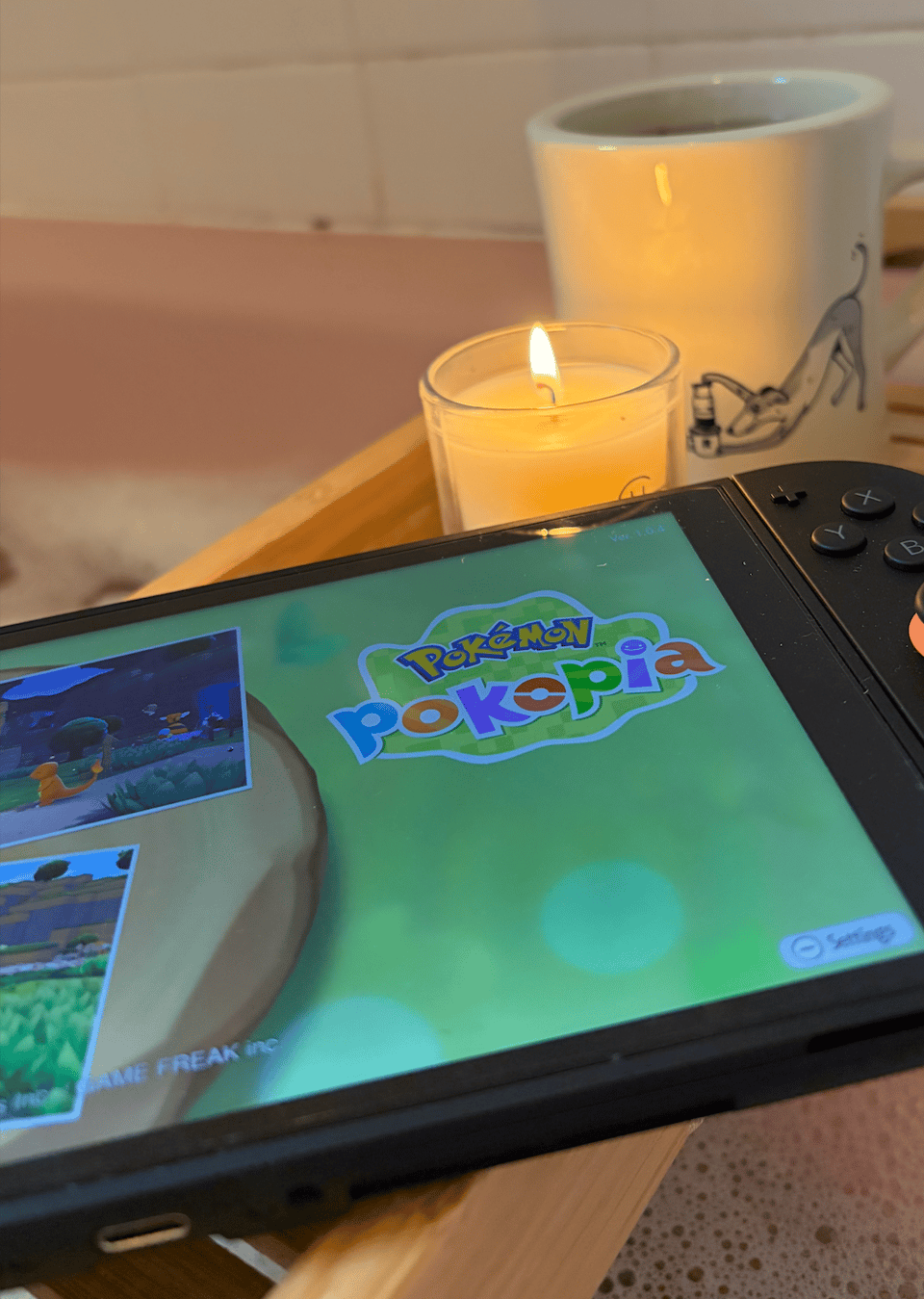 One of those bath shelves is in place over a bubble bath. It holds a cup of tea, a lit candle, and a Switch 2 displaying the Pokopia title screen.