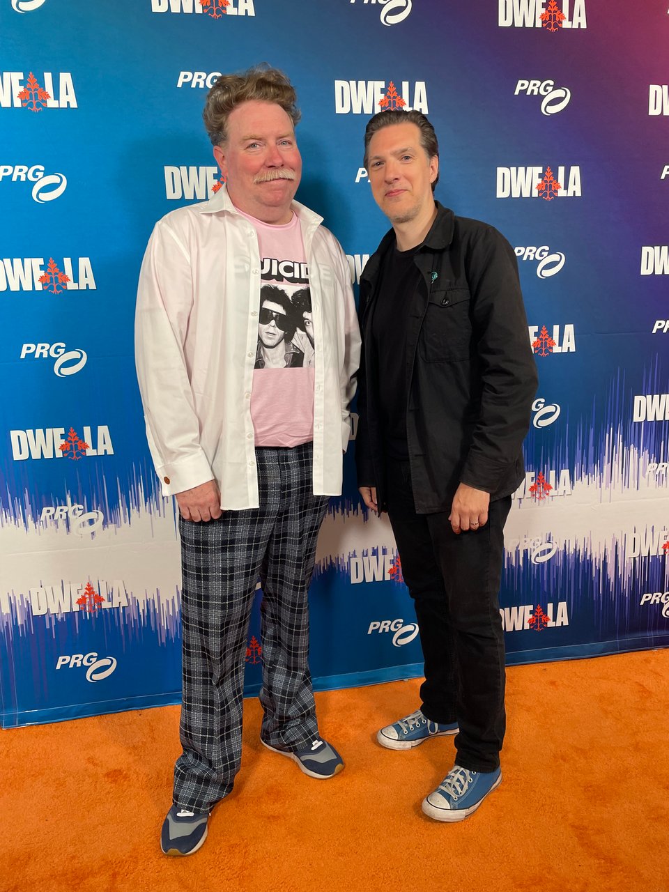 Two middle-aged men pose in front of a step and repeat