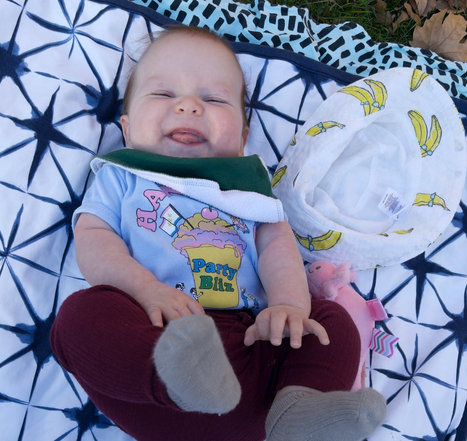 A baby on its back, laying on a blanket, smiling at the camera