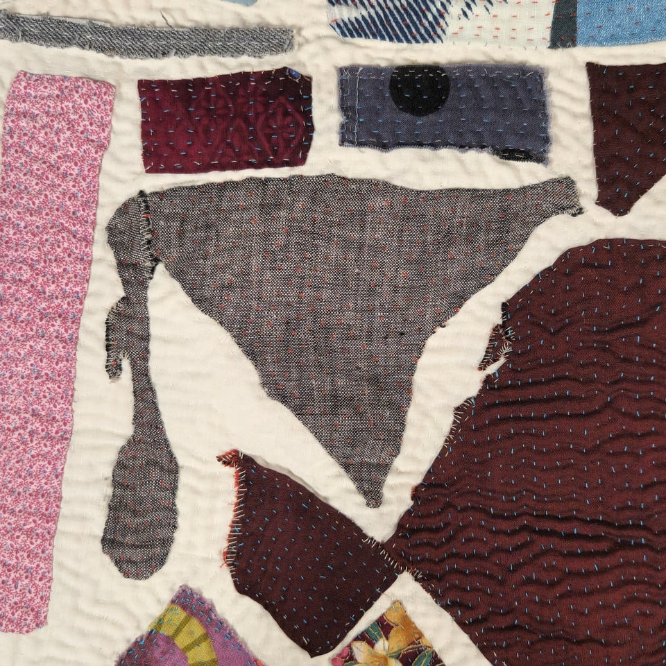 Detail view of Meet Me at the Corner in progress. This view has one piece of gray surrounded by pieces in different shades of gray and red. Sarah's hand stitching is visible.