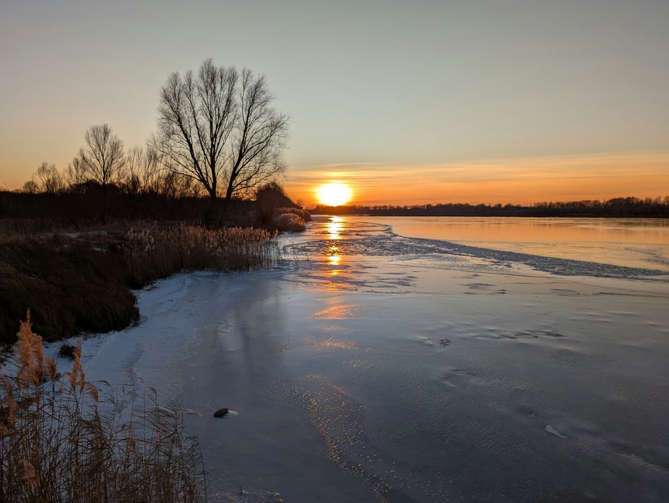 a frozen autumnal lakeshore with a glowing orange sunset