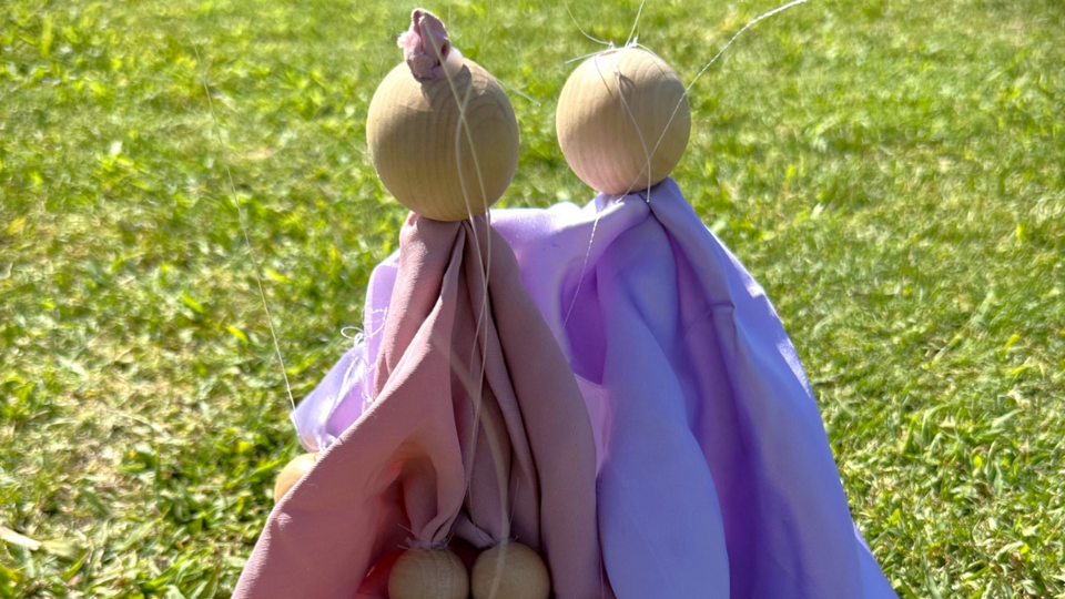 Two rough-made puppets of wooden balls and simple pastel cloth. One embraces the other gently.