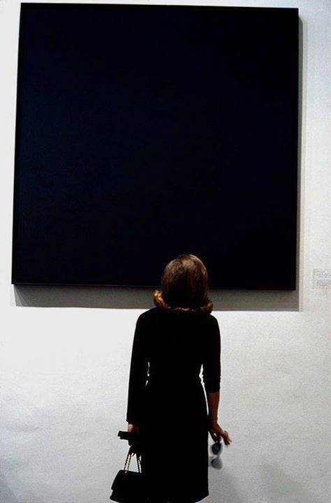 A woman wearing black looking at an all-black square canvas in a museum