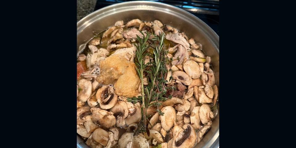 Top view of mushrooms, herbs, and a chicken carcass in a pot to make chicken stock
