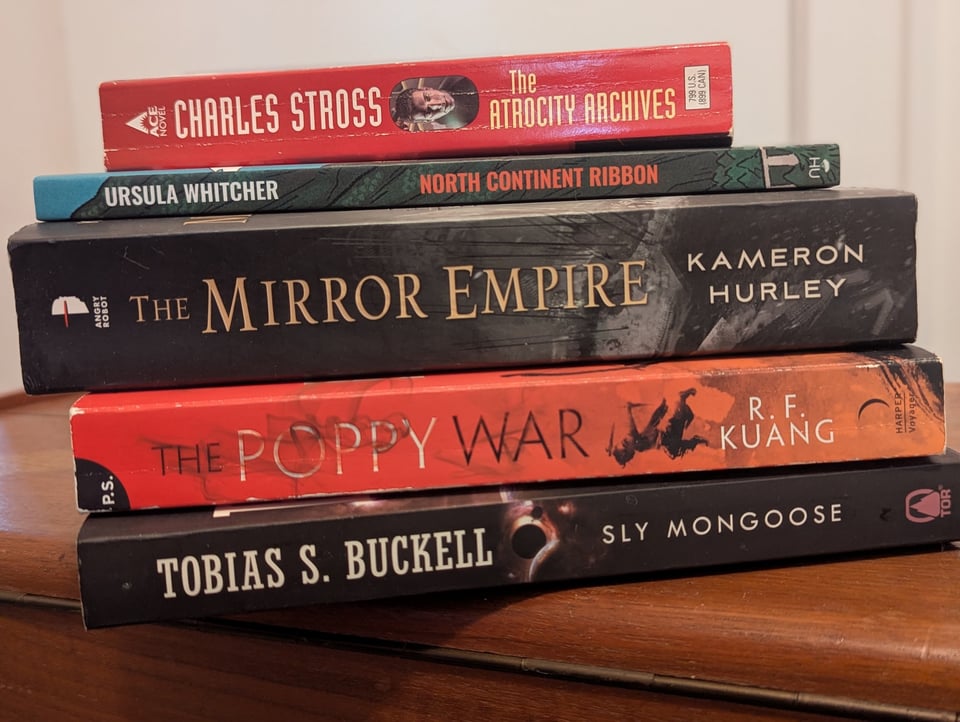 North Continent Ribbon stacked with books by Charles Stross, Kameron Hurley, R.F. Kuang, and Tobias Buckell