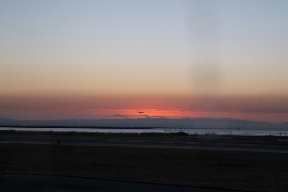 Image of the pre-dawn red sky, with a passenger plane silouetted in the distance just above the mountains and the clouds.
