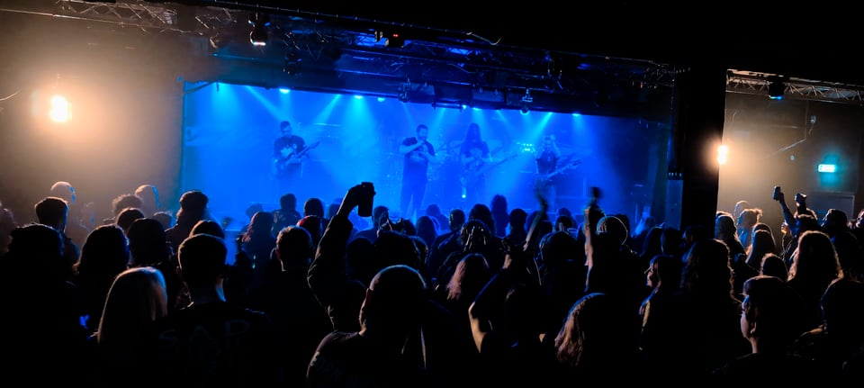 A photo of a band on stage lit up by blue lighting as a crowd cheers them