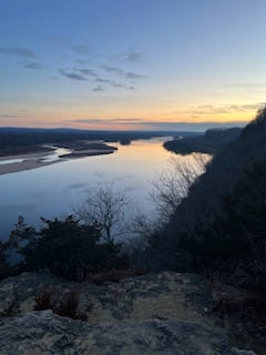 the view over Ferry Bluff at dusk with blue sky melting into residual sunset golds reflecting in the calm river below, framed by sandy brush and thin branches