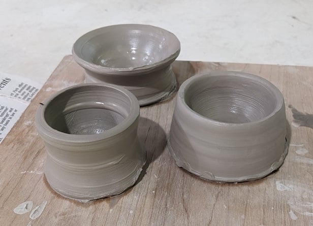 three small unfired clay bowls, still wet from slip, clustered together on a wooden board