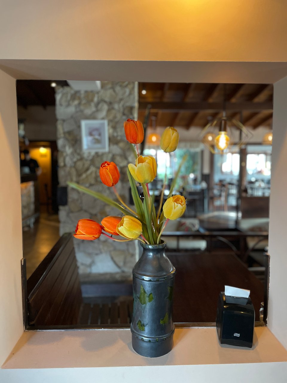 A vase of orange and yellow wooden tulips sits in an open windowless window frame looking into the restaurant.
