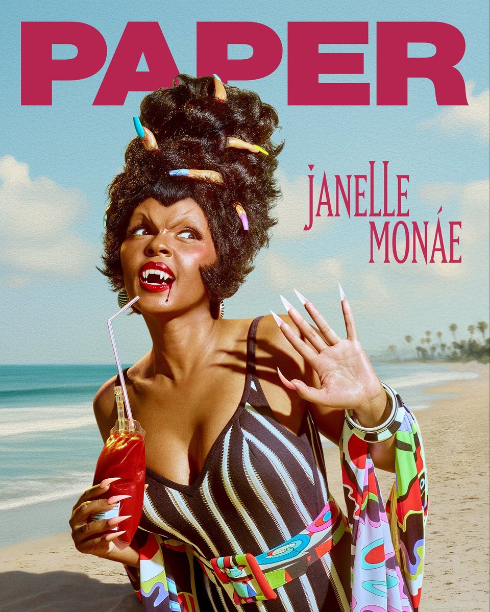 The cover of Paper magazine with Janelle Monae. She is dressed in colorful, retro but spooky outfits. Here she has a vampire face with built-up eyebrows and fangs, with a dribble of blood down her bright red lips. She wears a bathing suit and colorful scarf. Her hair is in a beehive with fingers tucked in, and she drinks from a blood bag.