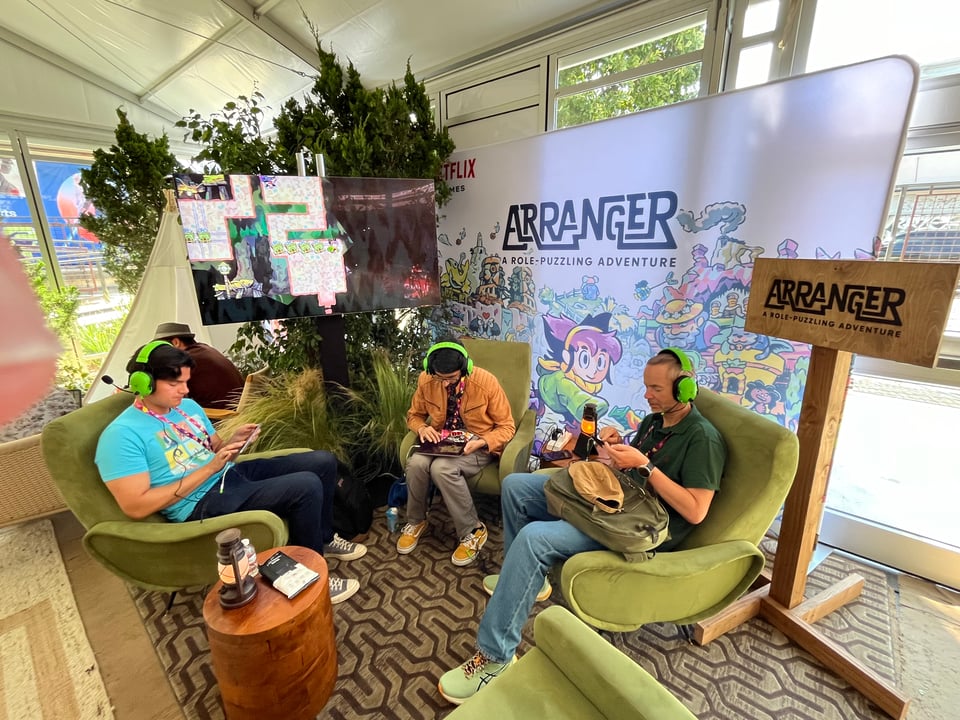 Three people playing Arranger on mobile devices in an Arranger-branded part of the Netflix tent at SGF