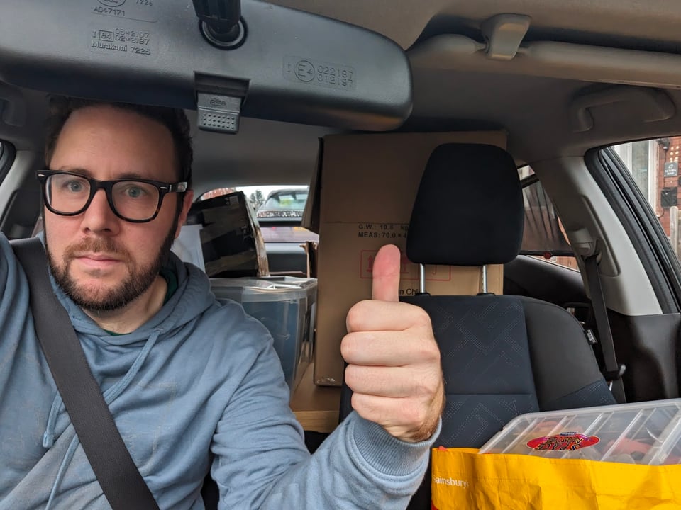 A picture of the author in a car full of boxes, with an unhappy-looking thumbs up