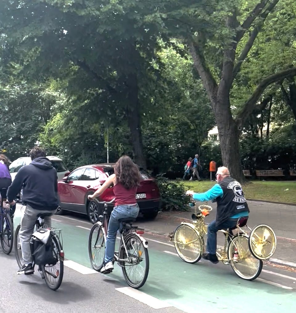 A bicycle all in gold in the stance of a laid-back motorcycle, with an elderly gentlemen in a black biker vest.