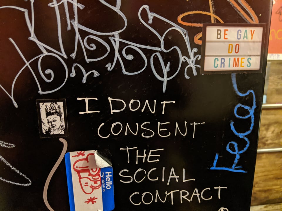 A photo I took of some graffiti (probably on a bathroom wall?) that says "I DON'T CONSENT THE SOCIAL CONTRACT" Also there's a BE GAY DO CRIMES sticker