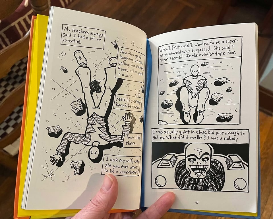 My hand holding open a copy of Lightning Man volume 1; the yellow endpapers are visible, as is the blue ribbon bookmark.