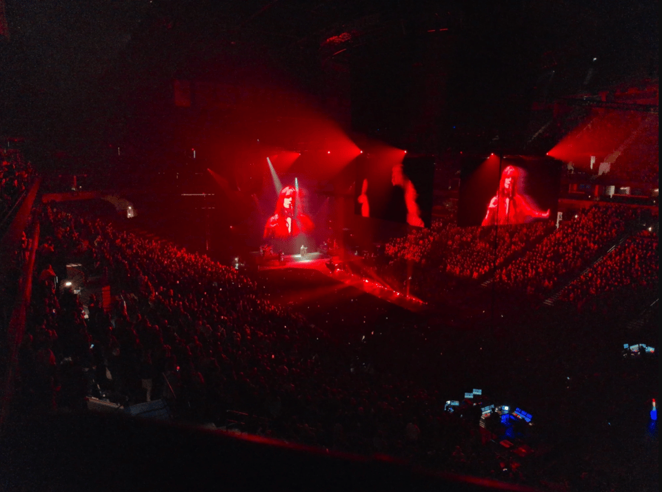 The inside of a darkened arena, lit with deep red lighting, with multiple screens hung from the rafters showing various images of the performers. It's very spooky.
