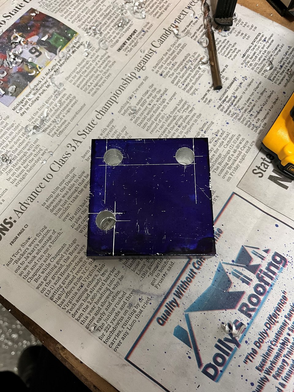 block of aluminum sitting on newspaper with three holes drilled out