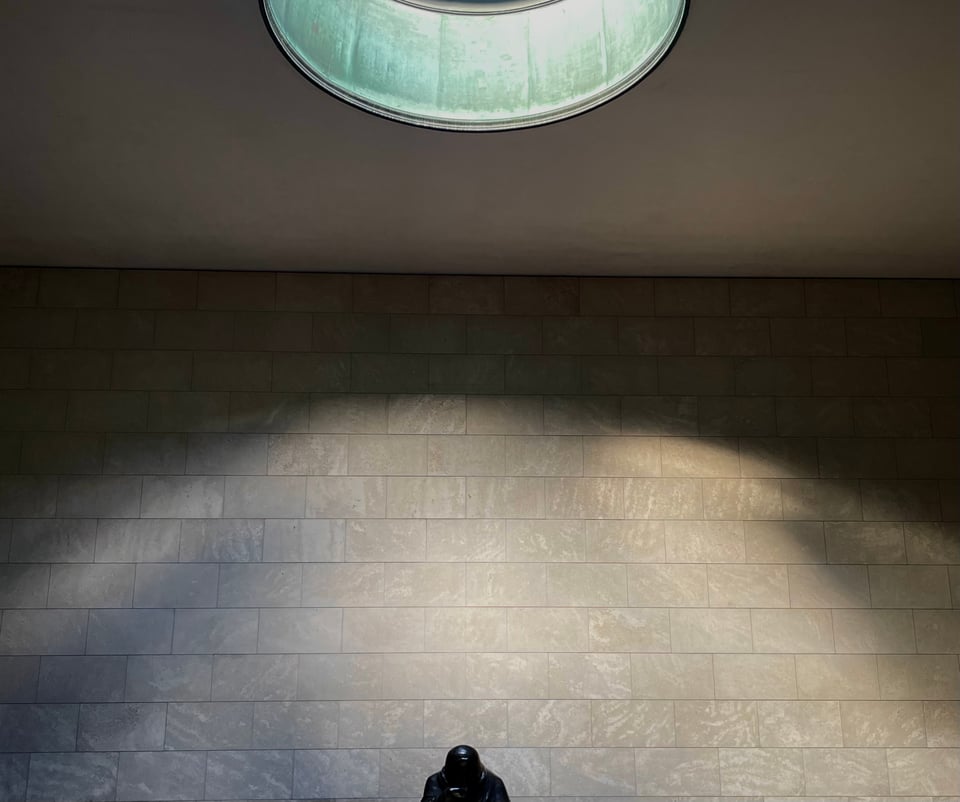 A view of the inside of the Neue Wache building in the Unter den linden boulevard in the centre of Berlin. The view is cropped to include part of the sky light and only part of the structure inside it. The skylight illuminates the wall behind in a convex shape, while the rest is darker
