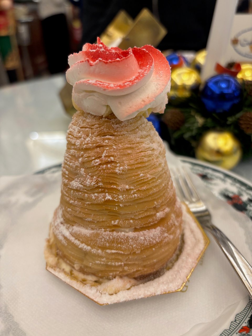 a pastry dusted with icing sugar and a flourish of pink cream on top