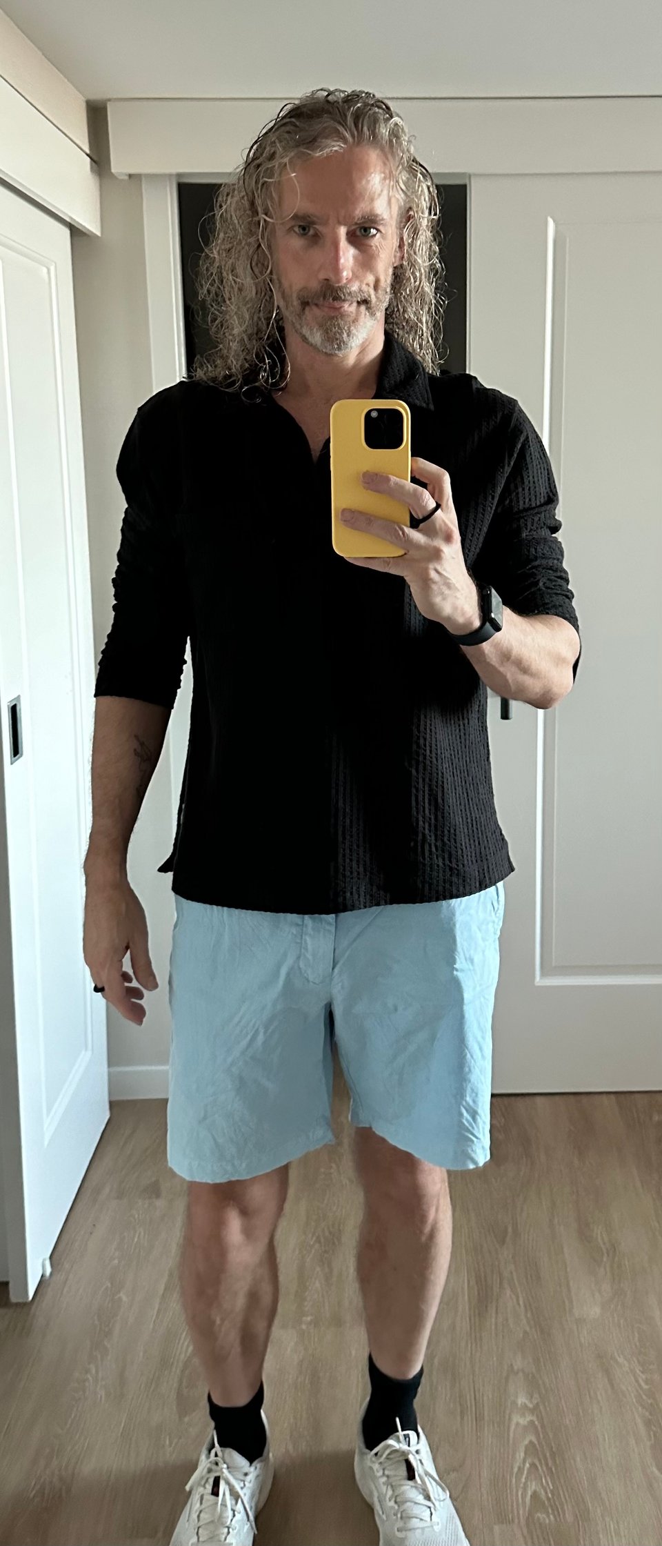 Full-body selfie in a hotel mirror of a white man with long hair, pale blue shorts, white sneakers, and a black seersucker pullover; he is smirking a little for the camera, but he doesn't realize that when he gets home in 13 hours, he will be a beaten-down, burned-out wreck of a man, having spent way too long driving (8+ hours that day)