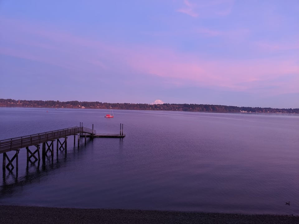 A sunset view across Puget Sound, with a mountain in the distance and a bright sailboat on the water.