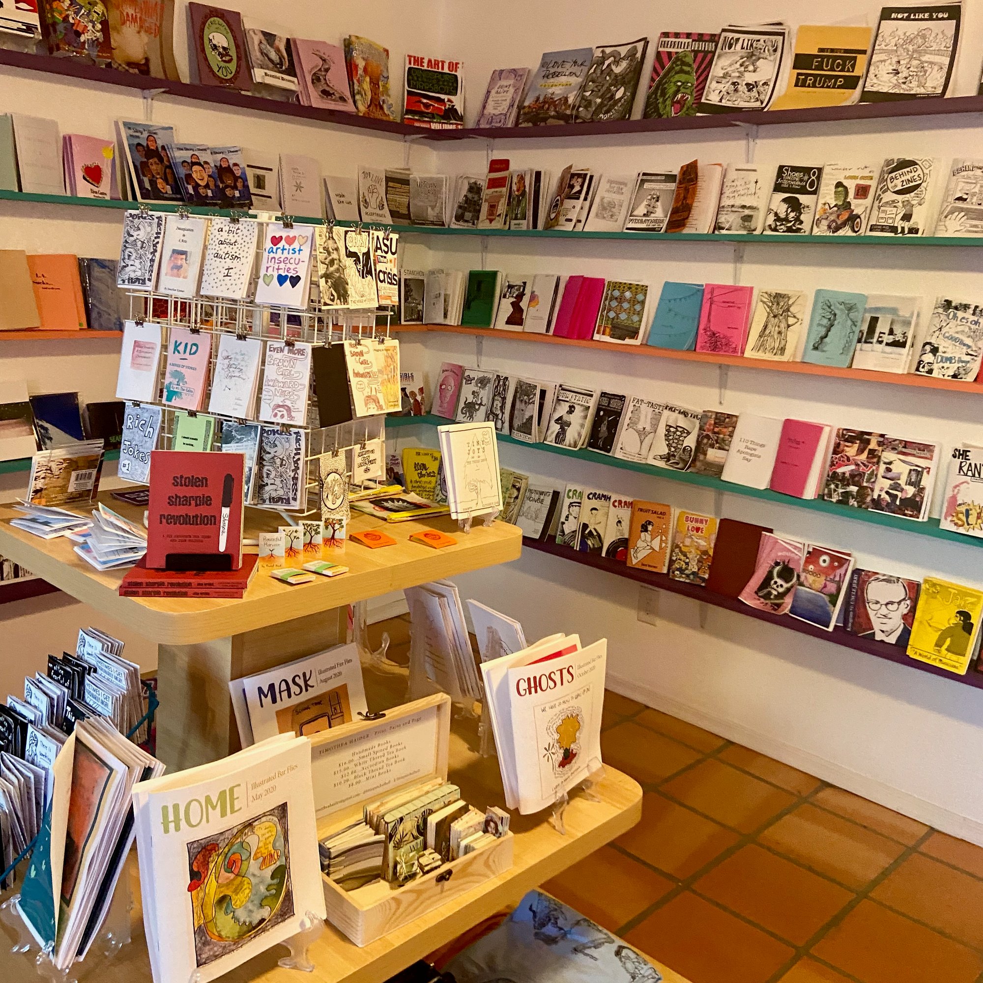 The inside display of zines in Wasted Ink Zine Distro. A central tiered table and shelves full of zines lining the walls.