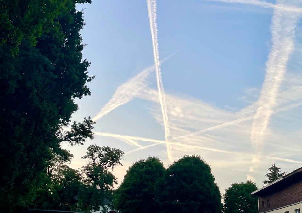A view of the sky without clouds, but with aeroplane condensation trails. Many, criss crossing, almost forming an asterisk