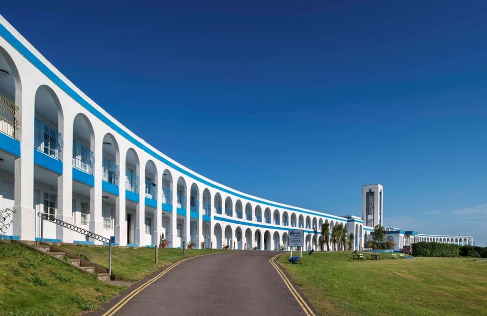 A sweeping white curve, two storeys high, leading to a tall thin tower. The curve contains balconies painted a bold blue.
