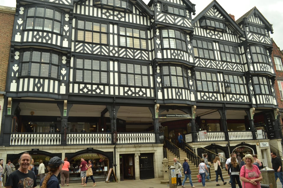 A large half timbered building with store fronts on the street and an elevated walkway with steps.
